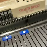 Blue needle position markers with arrows on a Silver Reed 3gg bulky knitting machine