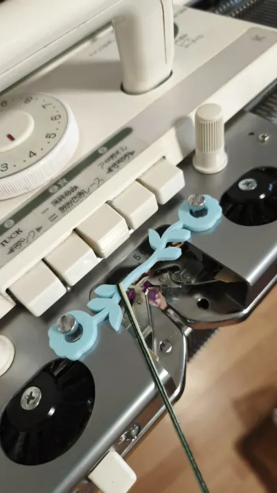 Blue plating yarn holder attached to a Brother standard gauge knitting machine